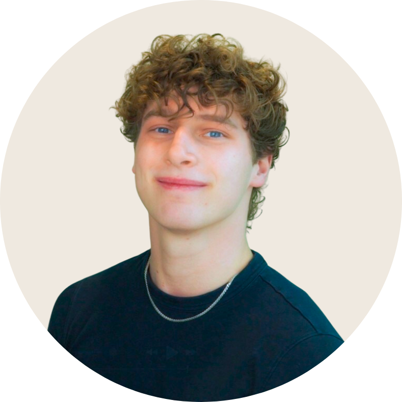 Een jongeman met krullend haar draagt een zwart shirt en een ketting om zijn nek.