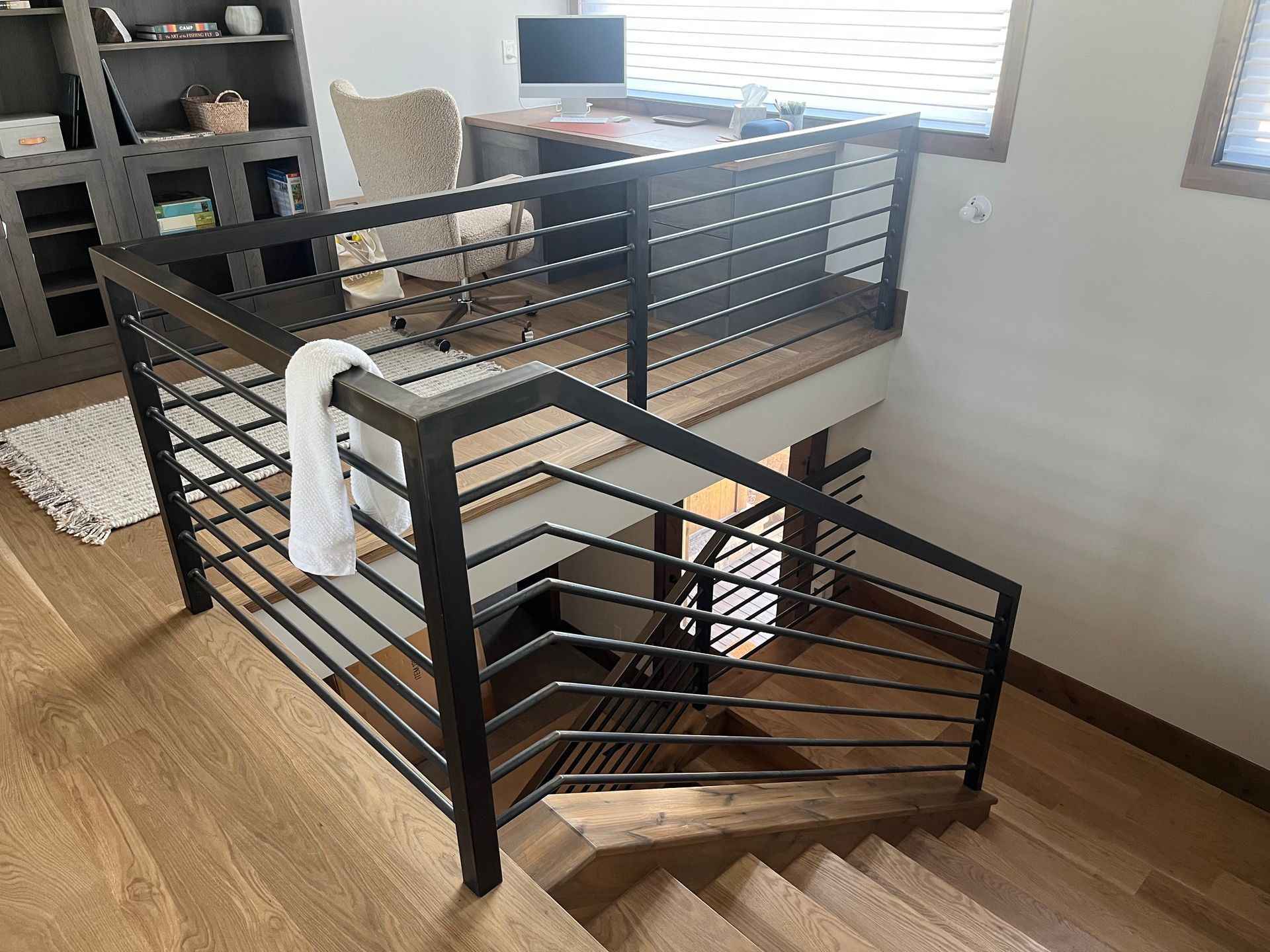 A wooden staircase with a metal railing and a desk in the background.