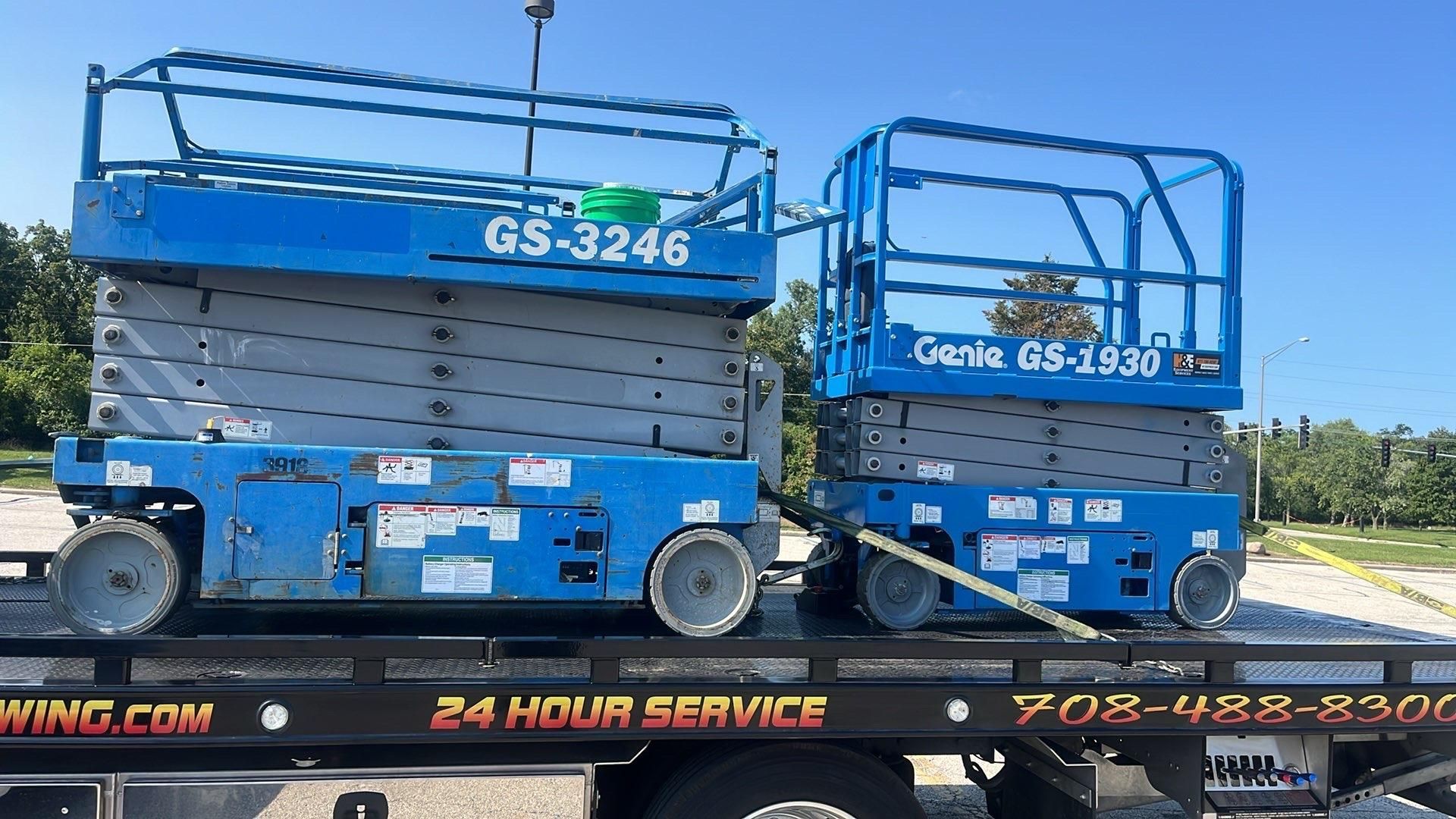 Blue Genie scissor lift on a flatbed trailer, parked outdoors under a clear sky.