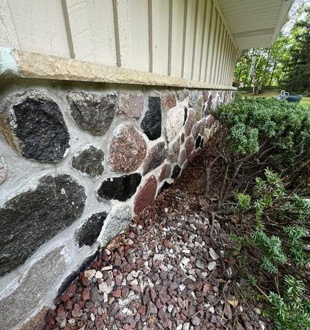 Stone foundation wall beside house with gravel and shrubs along the base