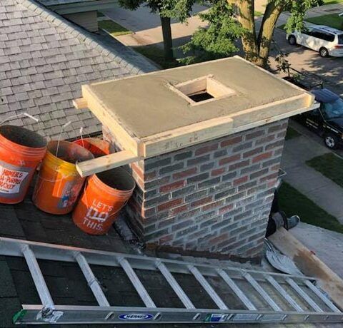 Roof chimney under construction with three orange buckets beside a ladder and shingles nearby