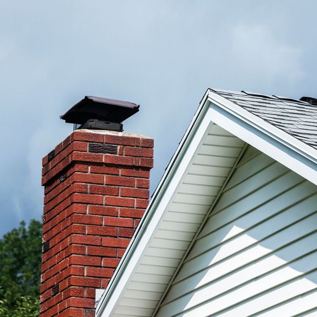 Brick chimney beside a white house roof under a cloudy sky