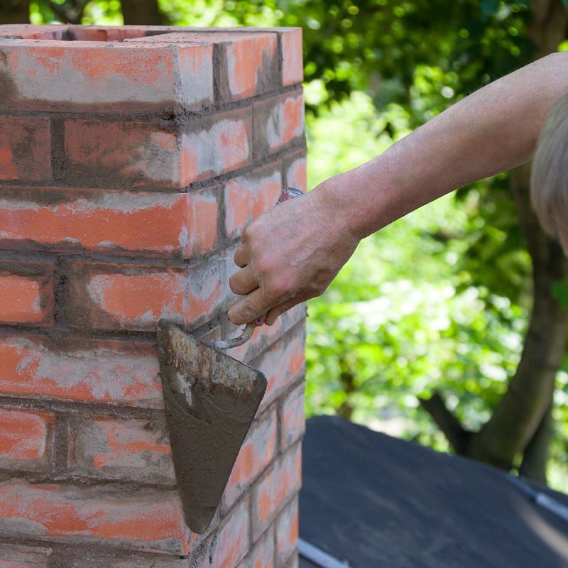 Hand trowel applying mortar to a red brick wall outdoors