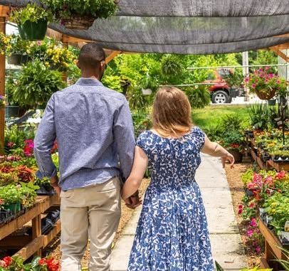 A man and a woman are walking through a greenhouse holding hands.