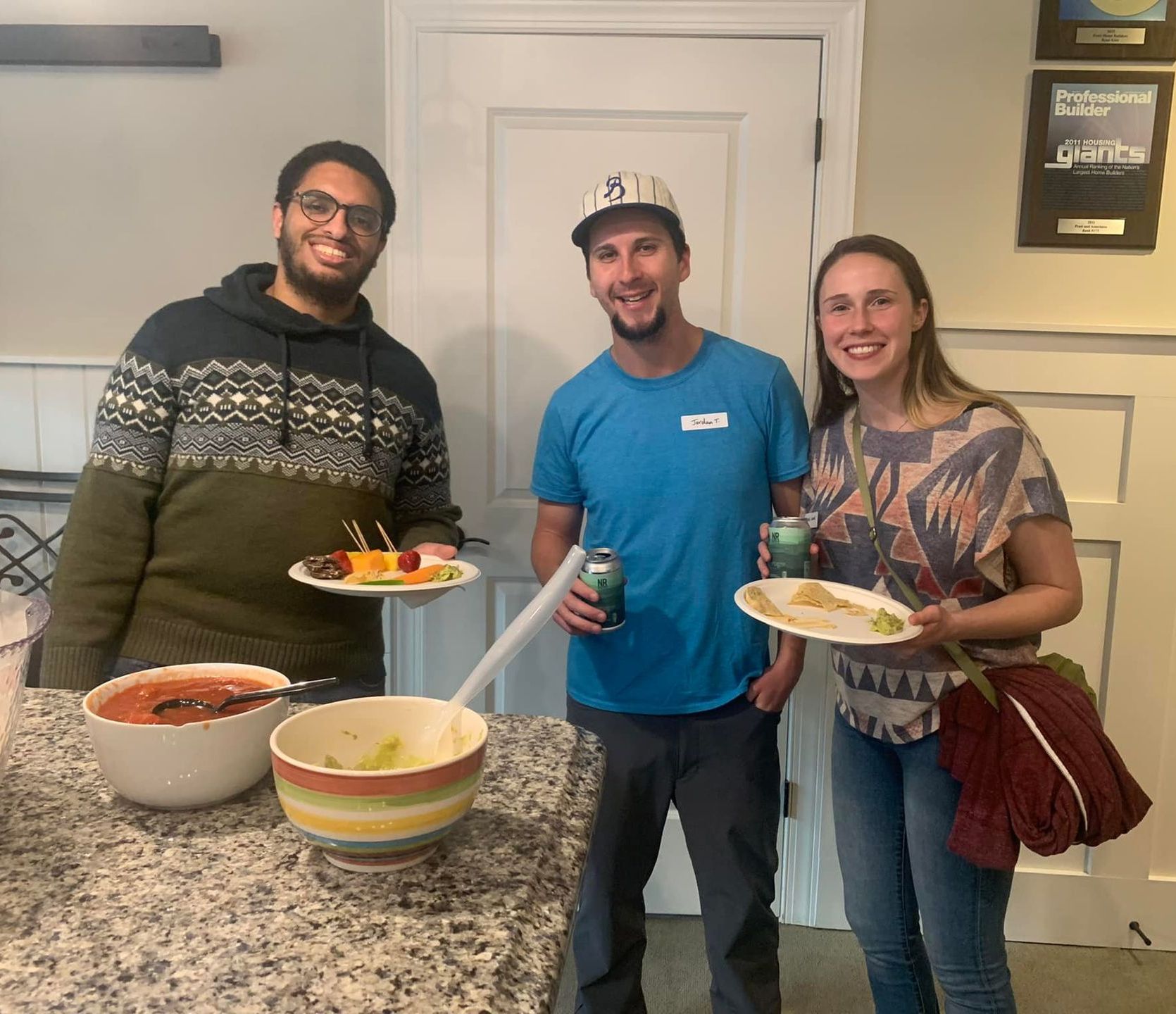 Three people standing next to each other holding plates of food