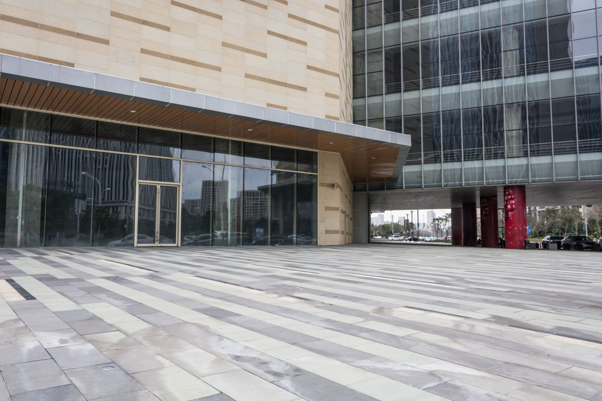 Modern building entrance with glass façade, tan stone walls, and wide tiled plaza in front
