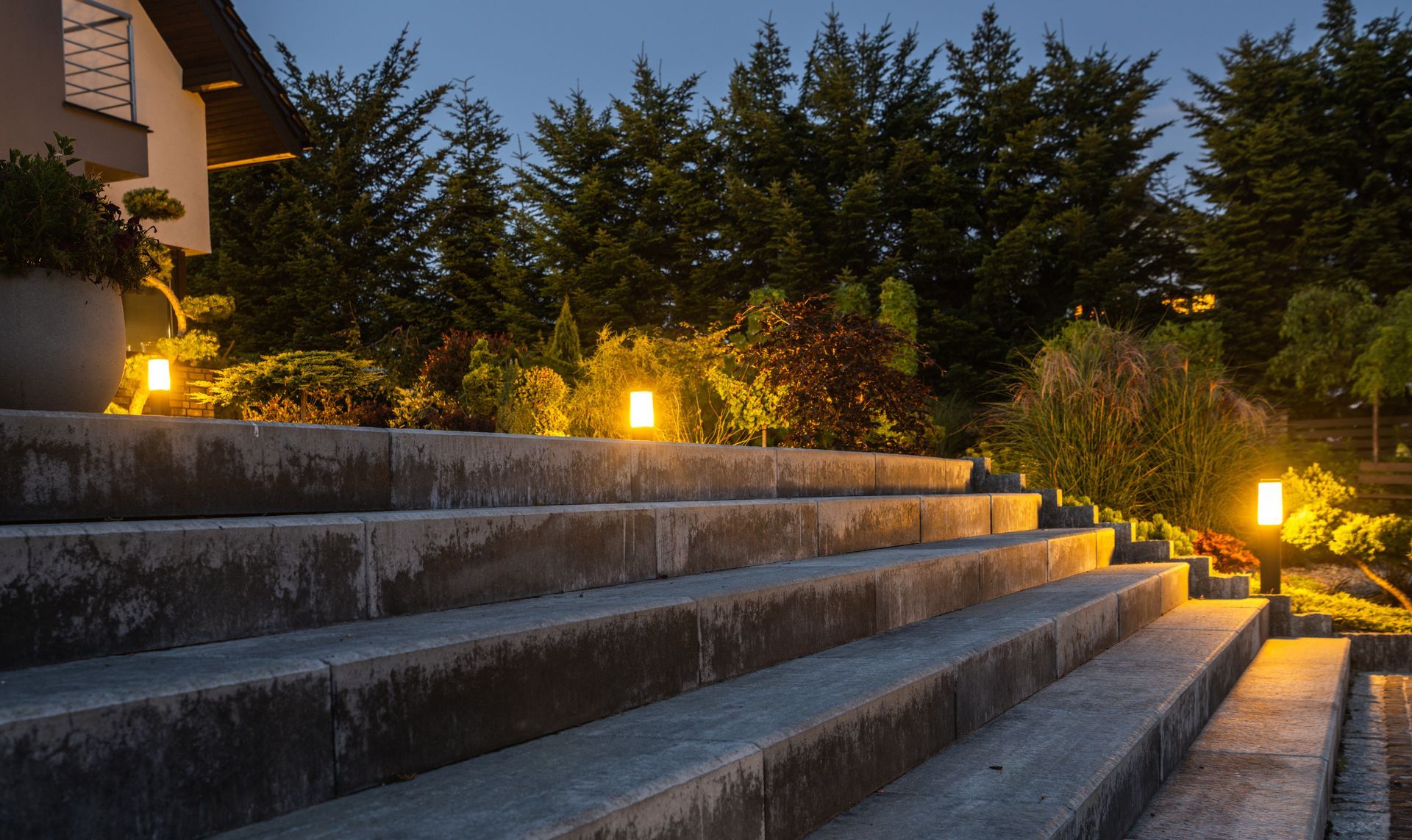 Stone steps leading to a landscaped garden at dusk, lit by warm pathway lights.