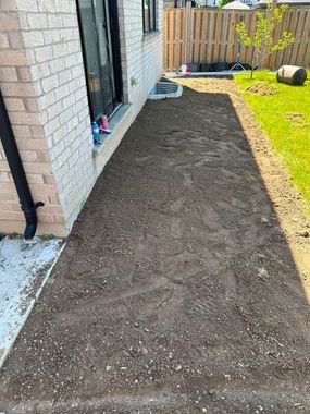 Newly landscaped gravel path beside a brick house, bordered by lawn and a wooden fence