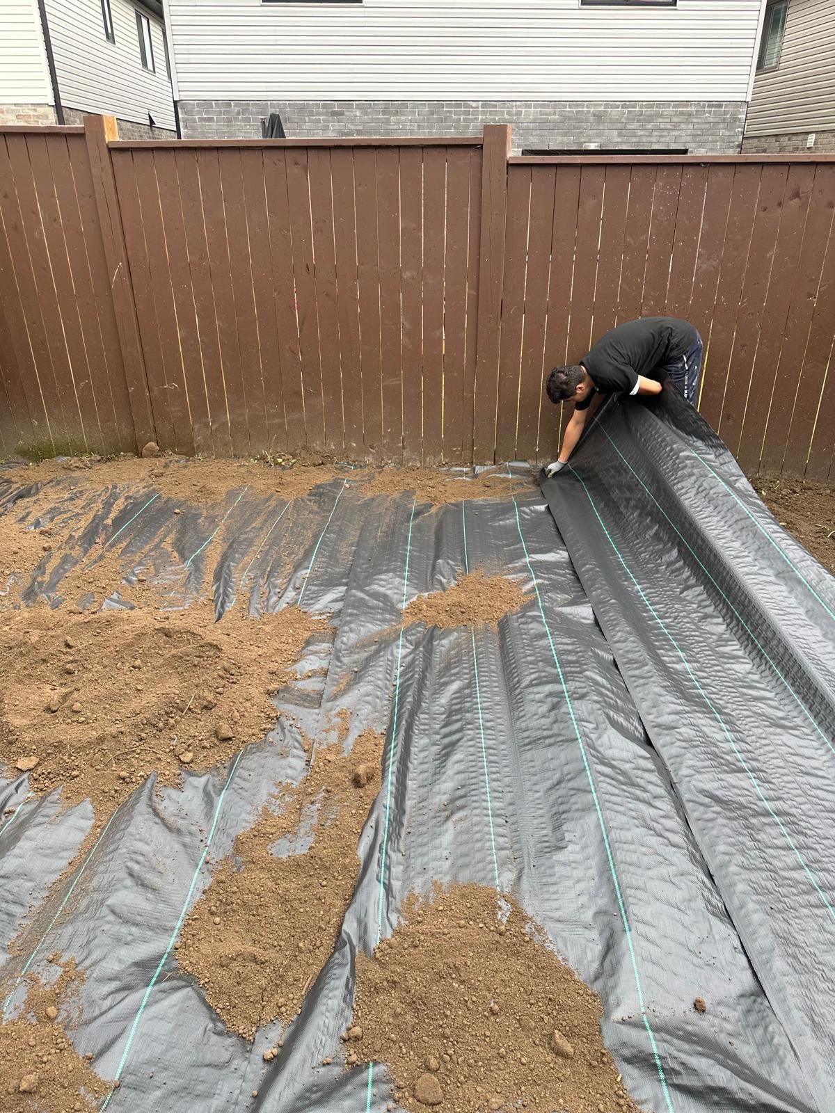 A man is laying a tarp over a pile of dirt in a backyard.
