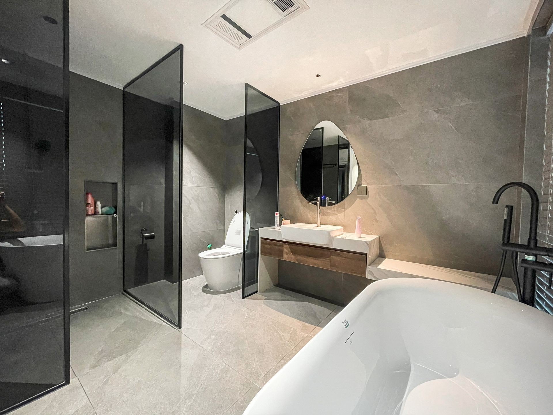 Modern bathroom with glass shower, toilet, floating vanity, round mirror, and freestanding tub