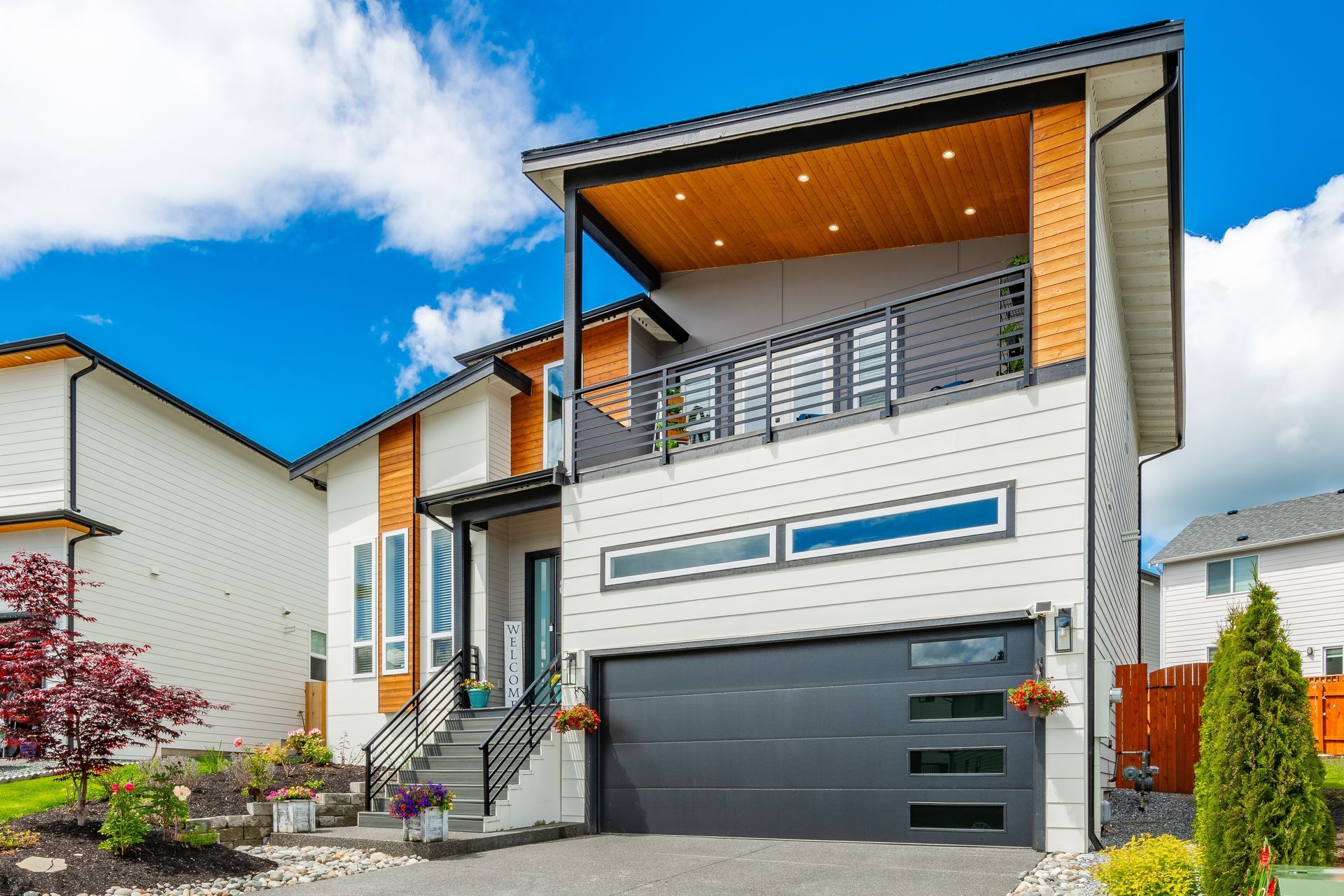 Modern two-story house with white siding, black garage door, and covered balcony under a blue sky