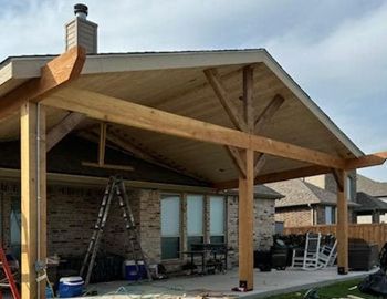 A wooden patio cover is being built in the backyard of a house.