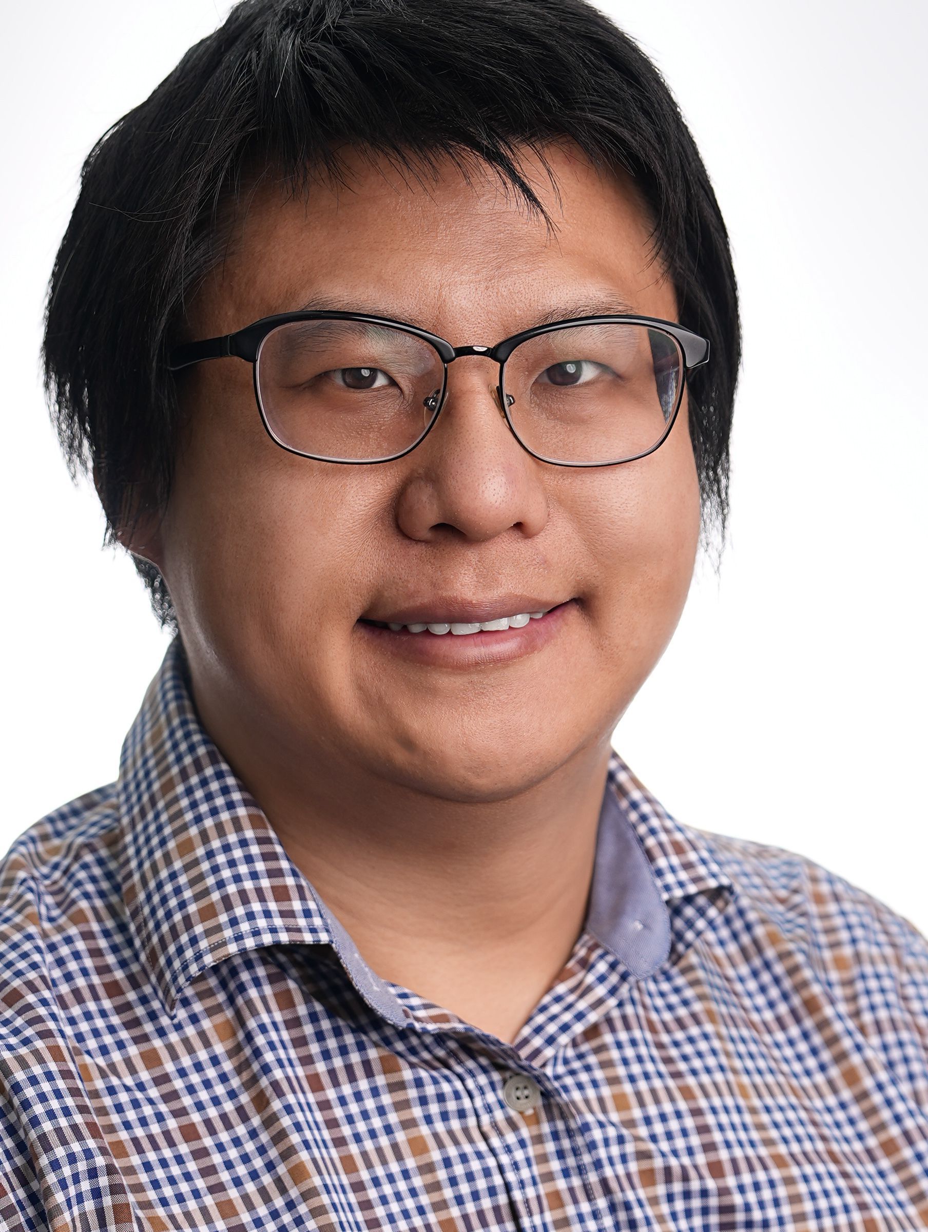 A man wearing glasses and a plaid shirt is smiling for the camera.