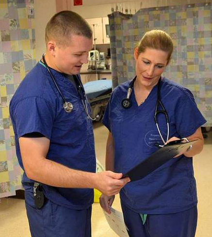 A man and a woman are looking at a clipboard in a hospital room.