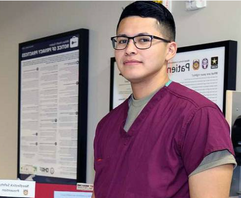 A young man wearing glasses and a purple scrub top