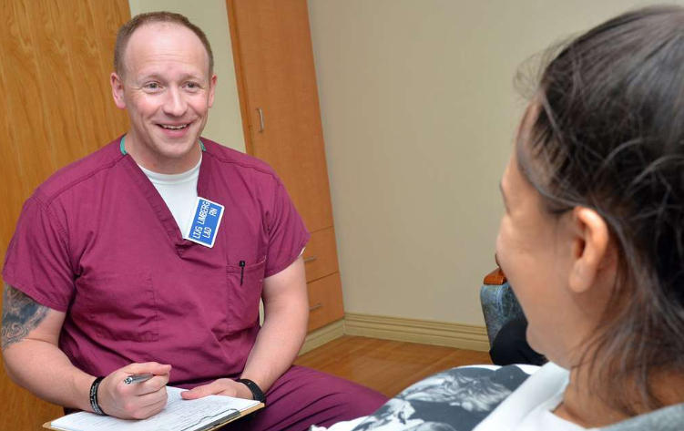 A man in scrubs is talking to a woman in a chair.