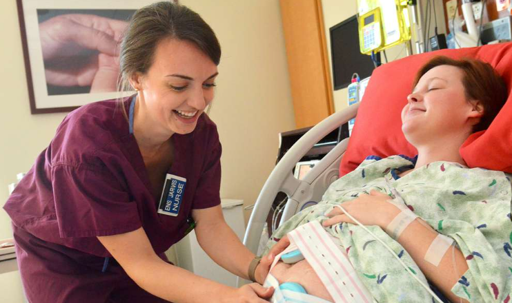 A nurse is talking to a pregnant woman in a hospital bed