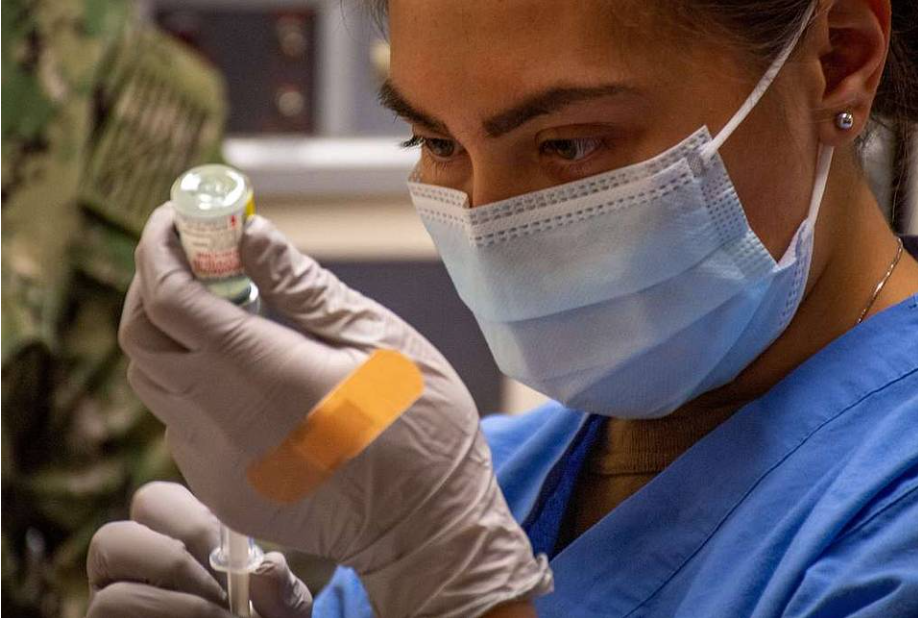 A nurse wearing a mask and gloves is preparing an injection.