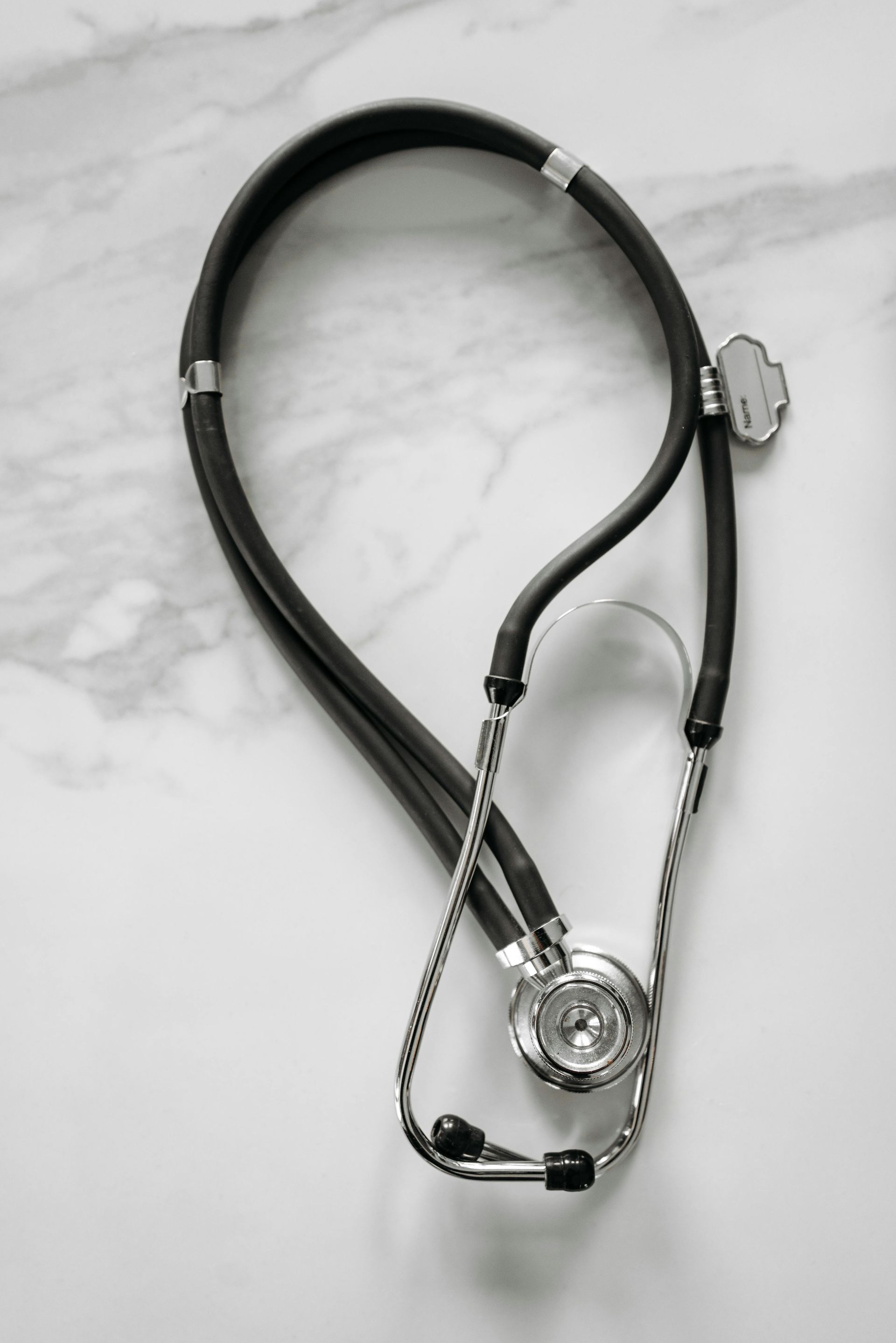 A black and silver stethoscope is laying on a white surface.