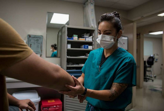 A nurse wearing a mask is holding a patient 's arm in a hospital.