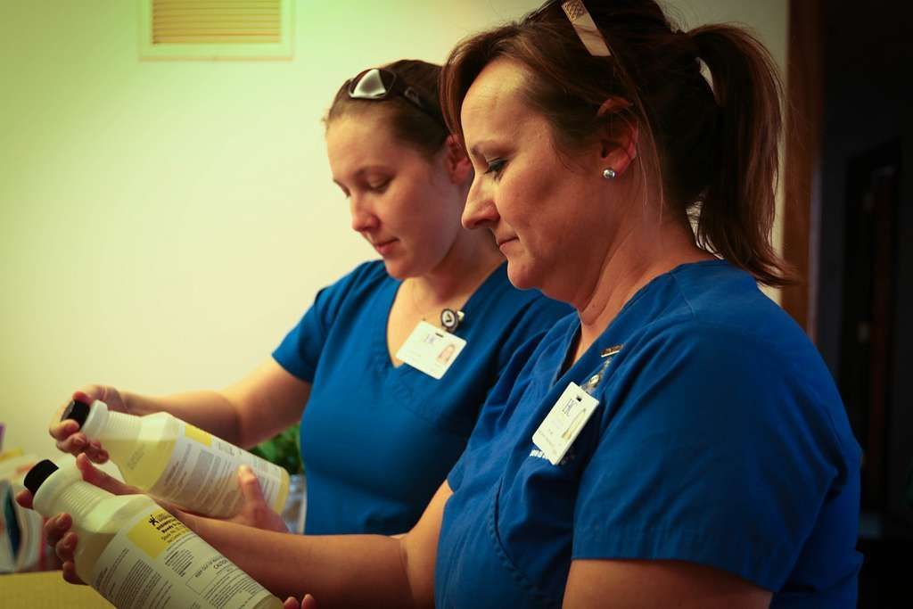 Two nurses in blue scrubs are looking at bottles