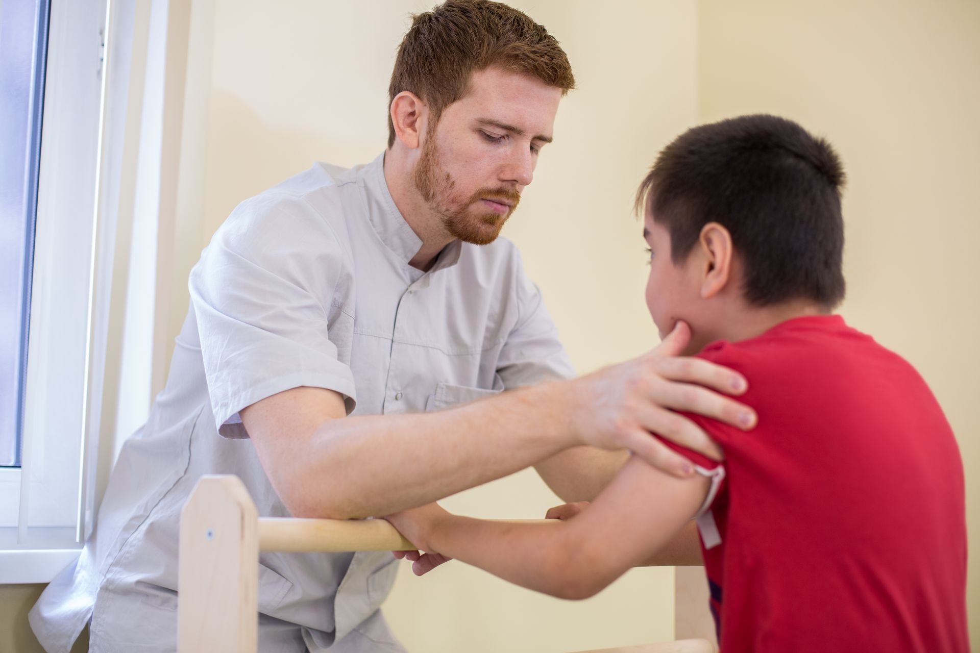 A man is helping a young boy with his arm exercises.