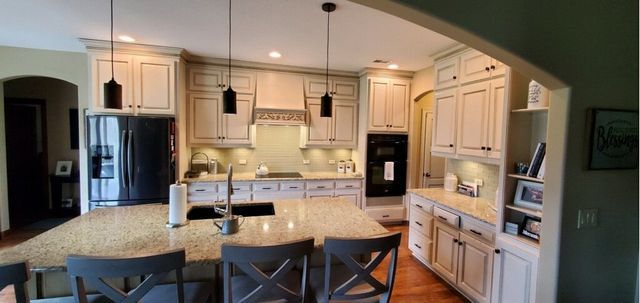 A kitchen with a large island, cream cabinets, and black pendant lights.