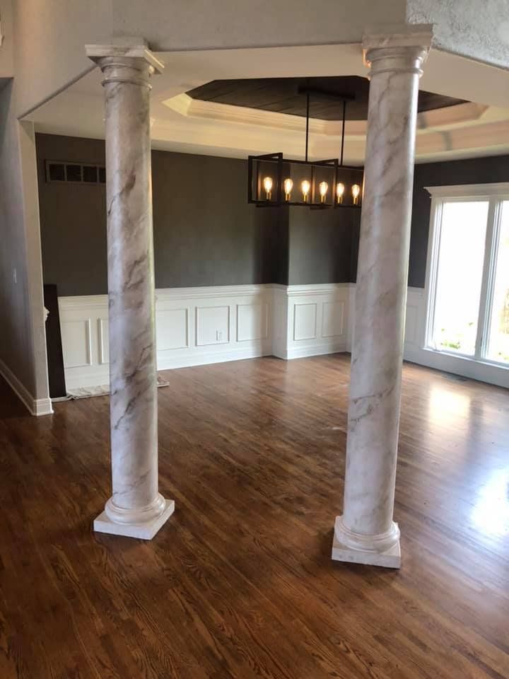 Two marble-look columns in a room with hardwood floors, leading to a dining area.