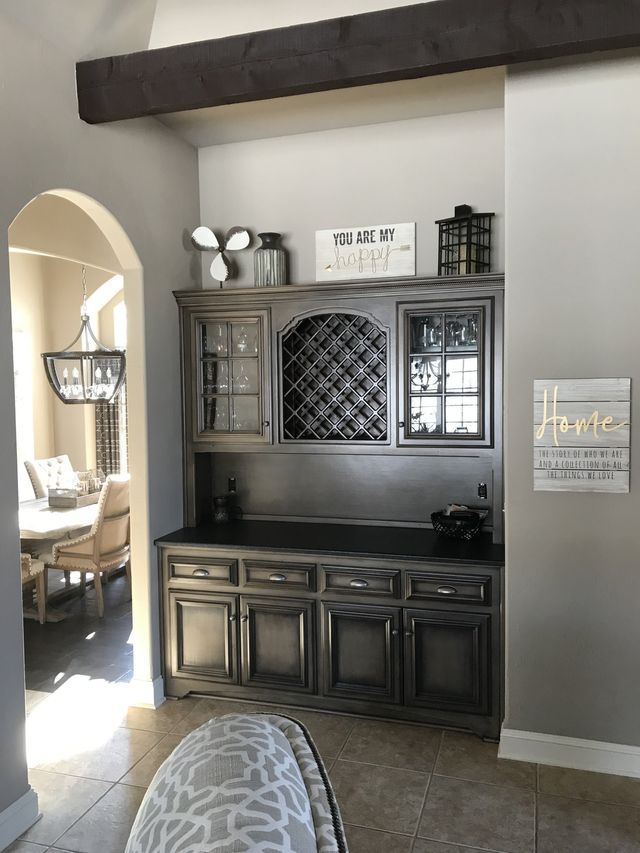 A built-in gray cabinet with a wine rack, decorations, and a wooden beam above, in a home.