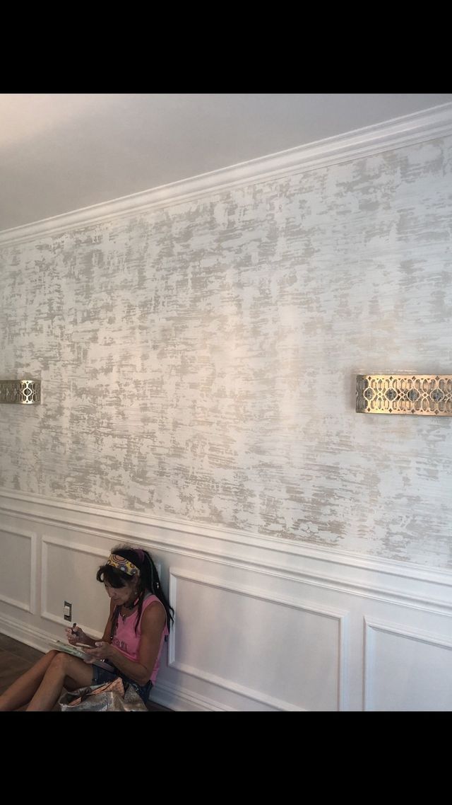 Girl sitting by white-paneled wall, textured silver-gray wall above.
