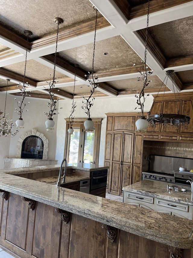 Kitchen with a granite countertop, wooden cabinets, and decorative ceiling beams with hanging light fixtures.