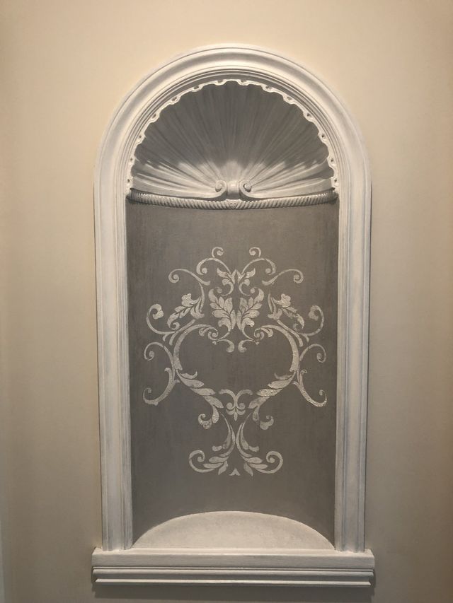 White decorative niche with arched top, ornate scrollwork design on gray background, shell-shaped detail.
