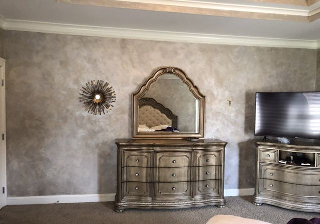 Bedroom with dresser, mirror, TV, and decorative wall art against a textured wall.