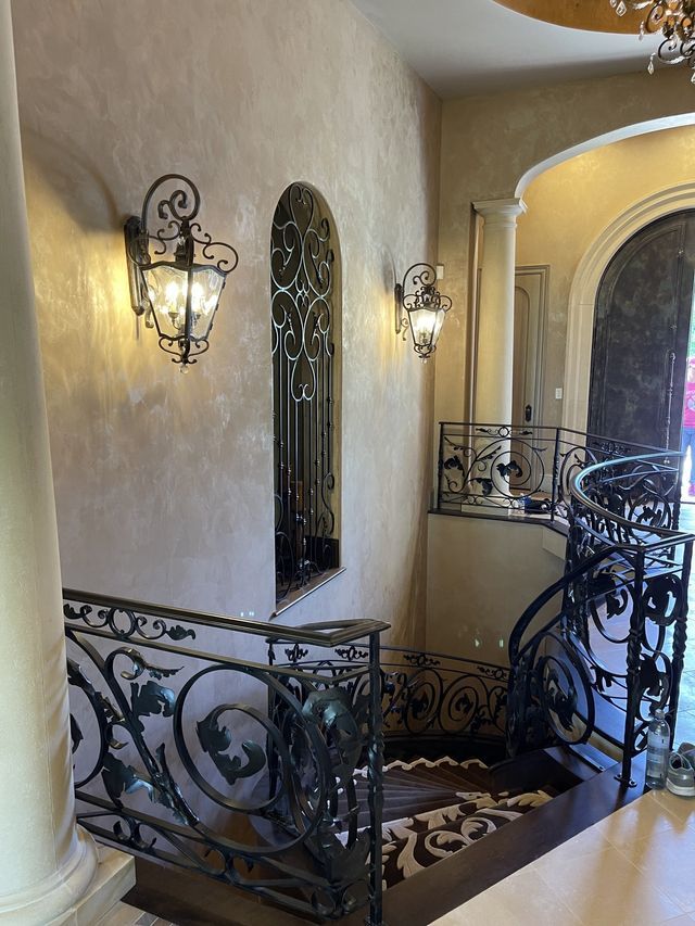 Ornate wrought iron staircase with sconce lighting and textured walls.