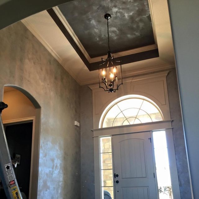 Entryway with a chandelier, textured gray walls, and a light-filled door.