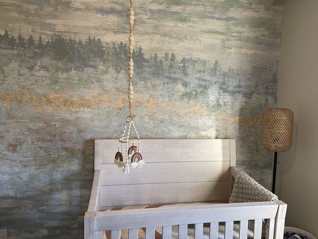 Crib with a white distressed finish, below a nature-themed mural. A macrame mobile hangs from the ceiling.
