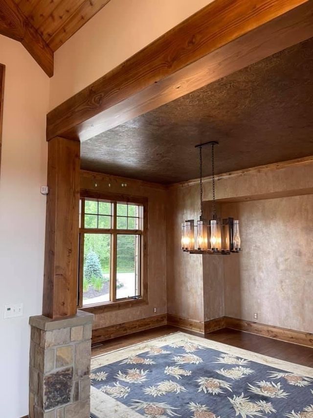 Interior room with wooden beams, large rug, chandelier, and a window overlooking greenery.