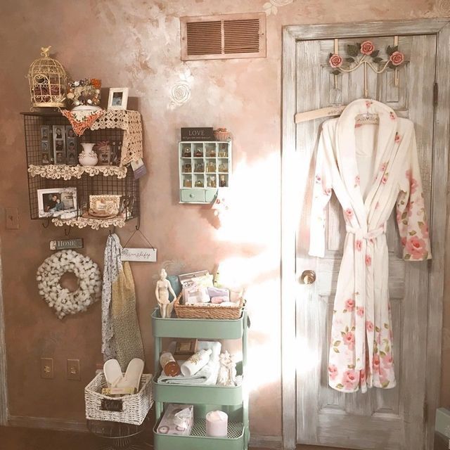 A shabby chic bathroom with a robe hanging on the door, shelves with decor, and a cart of toiletries.
