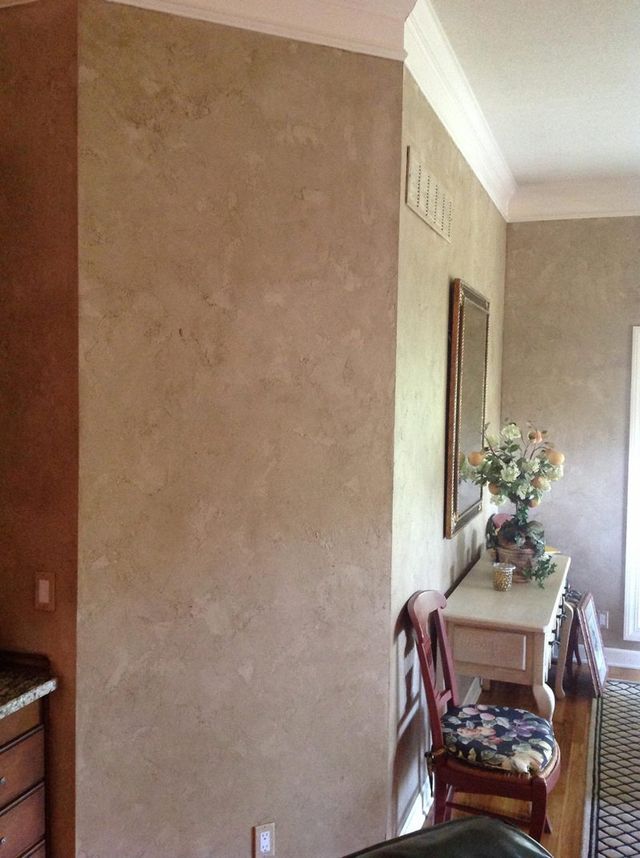 Tan textured walls in a room, with a white console table, flowers, and a chair.