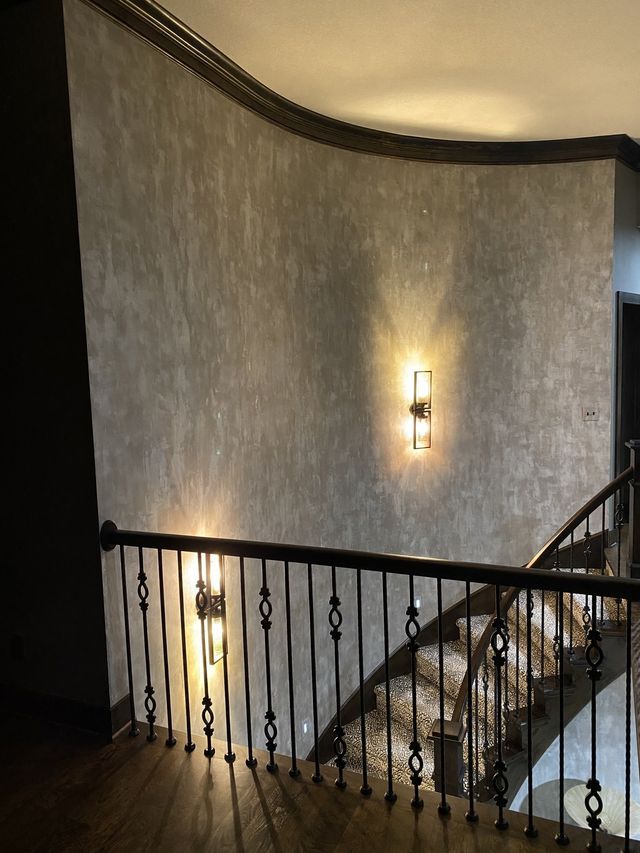 Curved staircase with textured wall, sconce lighting, and dark railing.