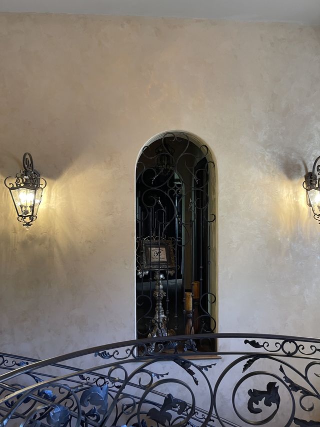 Interior with arched window, decorative ironwork, and sconce lighting. Beige walls with metallic effect.