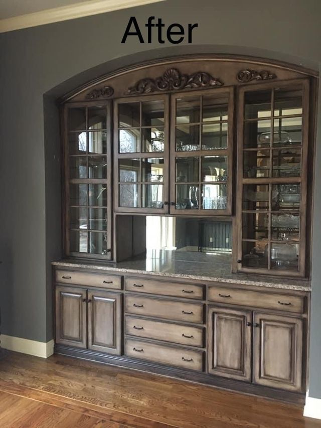 Wooden built-in cabinet with glass doors, drawers, and a granite countertop against a gray wall.