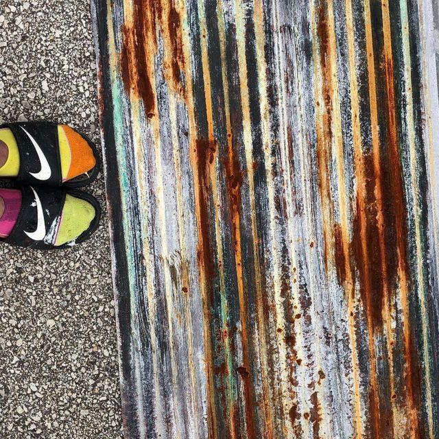 Colorful Nike slides next to weathered, rusted corrugated metal.