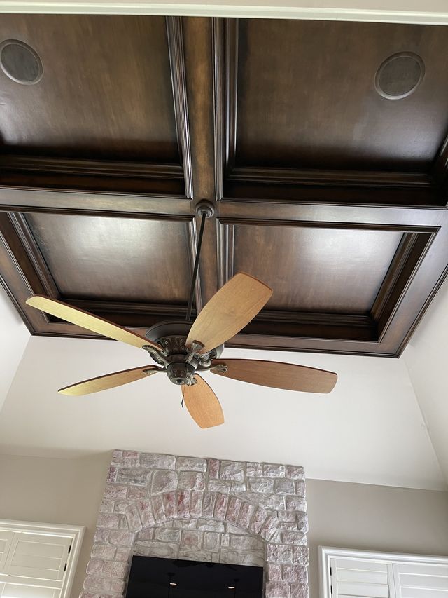 Dark stained coffered ceiling with a ceiling fan; white brick fireplace below.