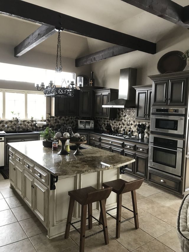 Kitchen with island, dark cabinets, granite countertops, stainless steel appliances, and wooden beams.