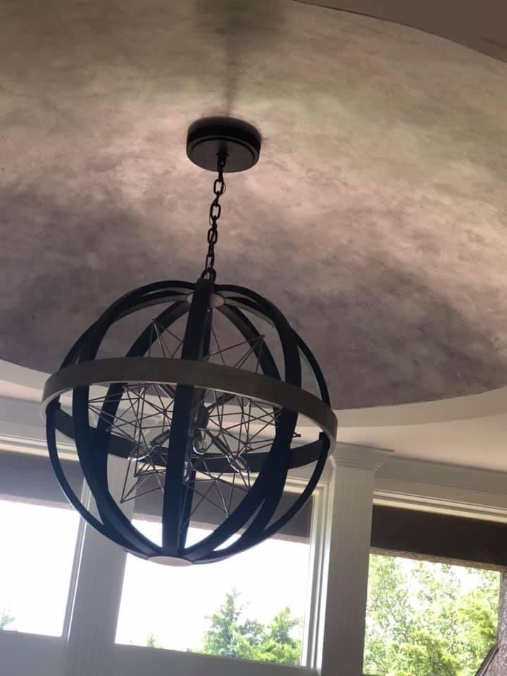 Orb-shaped pendant light hanging from a decorative ceiling. Light has a dark metal frame and a chain.