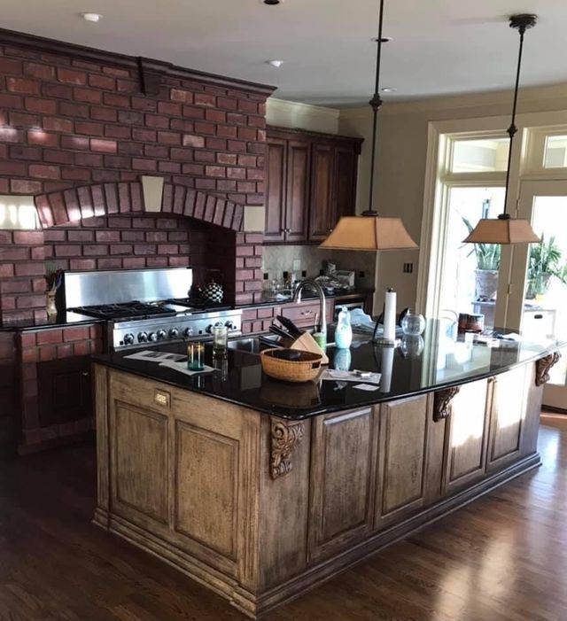 Kitchen with brick accent wall, wooden island, dark countertops, and pendant lights.