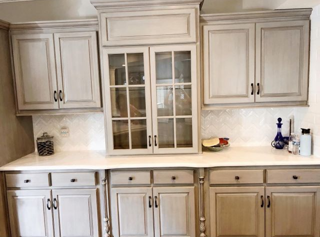 Kitchen cabinets in a light gray color with dark hardware, white countertops, and a glass-front cabinet.