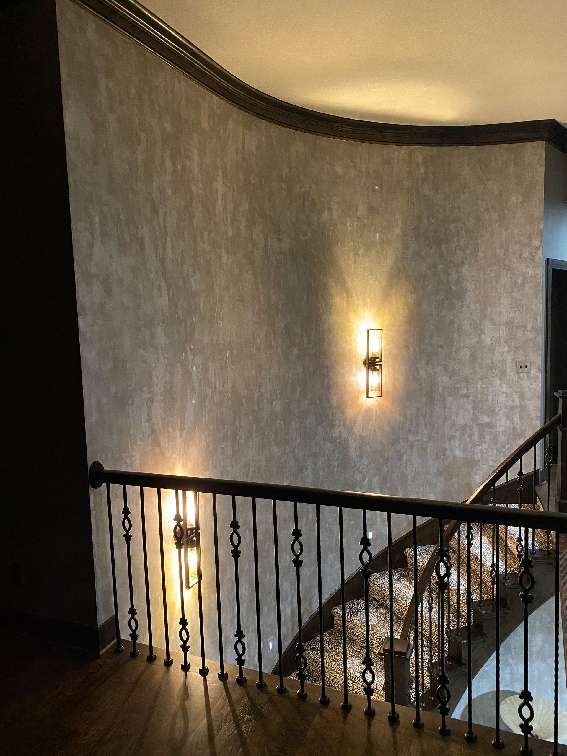 Curved staircase with black railing and wall sconces in a dimly lit interior hallway