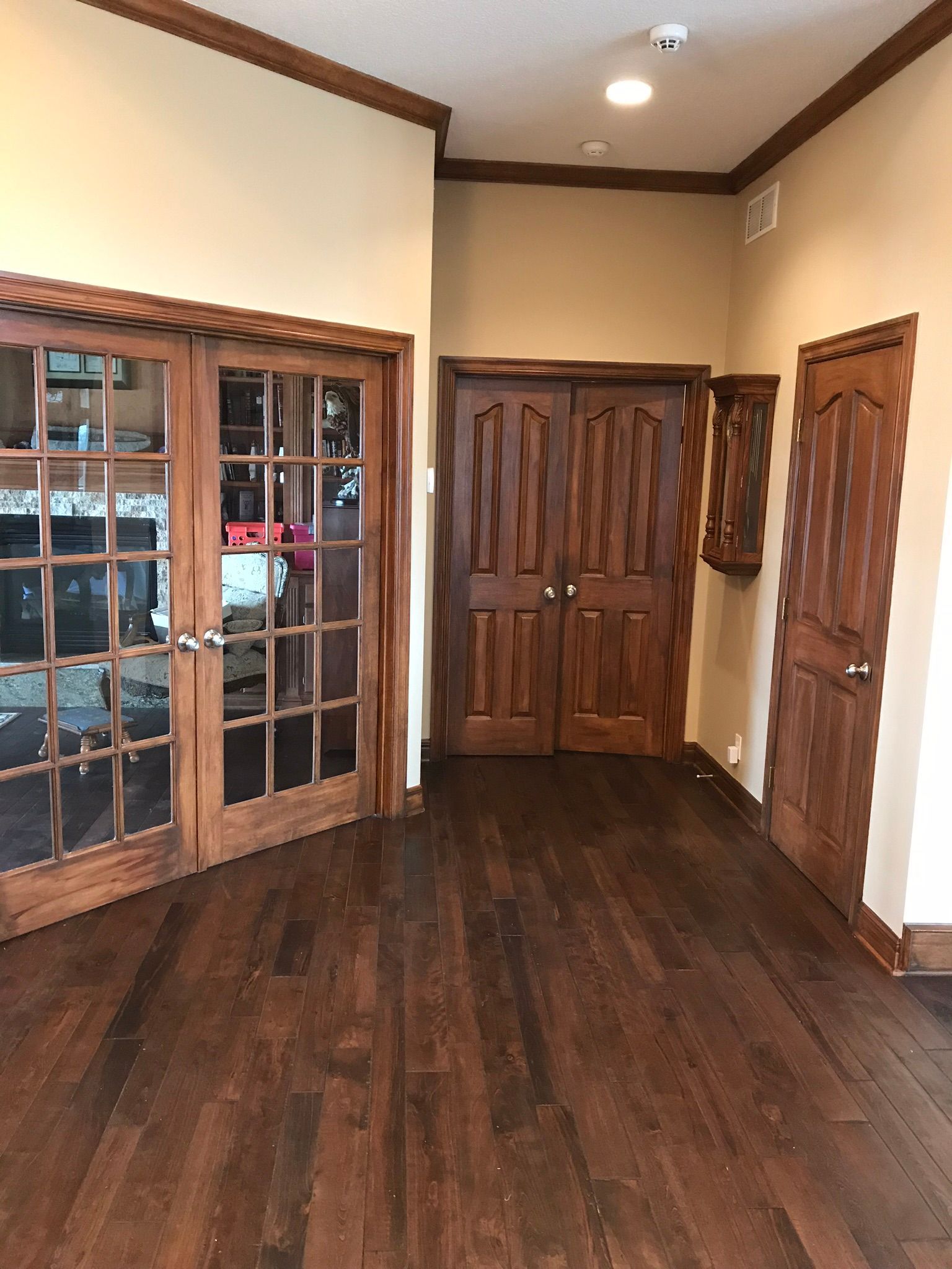 Empty hallway with dark wood floors, paneled doors, and a glass-front cabinet on the left.